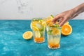 Refreshing detox water with lemon, orange, mint in glasses wiht hand on white blue background, summer homemade lemonade Royalty Free Stock Photo