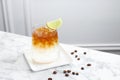 Refreshing espresso tonic drink with slice of lime and coffee beans on white marble table Royalty Free Stock Photo