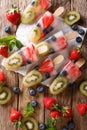 refreshing fruit popsicle lollies with berries, fruits peppermint on wooden background. Vertical top view