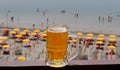 A refreshing glass of beer over a beach resort with parasols and people bathing