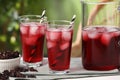 Refreshing hibiscus tea with ice cubes and dry roselle flowers on white table against blurred green background