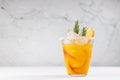 Refreshing juicy peach cocktail with ice, rosemary, sugar rim, fruit slices in misted glass on white wood table, concrete wall.