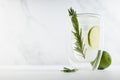 Refreshing  mojito cocktail with ice cubes, lime slices, green rosemary twig, ingredients in elegant modern white interior. Royalty Free Stock Photo