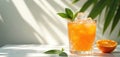 Refreshing orange drink glass with ice cubes mint leaves and orange slice. Sunlight and shadow create the mood on white table. Royalty Free Stock Photo