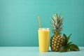 Refreshing pineapple juice and whole pineapple on turquoise background with copy space