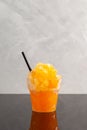 Refreshing Slushie drink on dark glass table. Orange Granizado in disposable plastic cup. Sweet citrus Shaved ice. Take away food Royalty Free Stock Photo