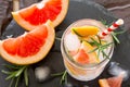 Refreshing summer drink with ice with rosemary and grapefruit on a stone background.