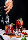 Refreshing summer drink with strawberry slices, lime, and mint leaf in glasses , hand put ice on dark background beverage soda