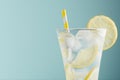 Refreshing summer tonic water with lemon, ice cubes, yellow straw in light soft pastel blue color background, closeup, half, top.