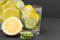 Water with lemon and cucumber and mint in a glass cup and in a jug next to half a fresh lemon and cucumber slices on a black backg Royalty Free Stock Photo