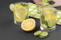 Water with lemon and cucumber and mint in a glass cup next to half a fresh lemon and cucumber slices on a black background