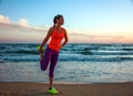 Fit woman in sports gear on beach at sunset stretching