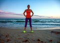 Fit woman standing in sports gear on beach at sunset