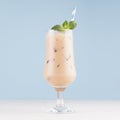 Refreshment baileys creamy cocktail in misted elegant wineglass with ice cubes, green mint, straw in light blue interior. Royalty Free Stock Photo