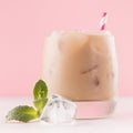 Refreshment baileys creamy cocktail in misted glass with ice cubes, green mint, straw in pink interior on white wooden table.