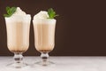 Refreshment coffee drink with fresh green mint, whipped cream, foam in two glass in luxury dark brown interior on white wood table