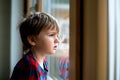 Refugee little kid boy looking in the window with hope. Save Ukrainian children. Alone child waiting for paren