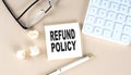 REFUND POLICY text on sticky with pen ,calculator and glasses on a beige background