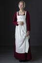 A Regency maid servant wearing a red linen dress with an apron and cap against a studio backdrop