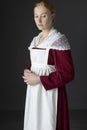 A Regency maid servant wearing a red linen dress with an apron and a lace modesty shawl against a studio backdrop