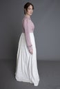 A Regency woman wearing a cream embroidered dress and a pink linen short spencer