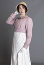 A Regency woman wearing a cream embroidered dress and a pink linen short spencer