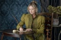 A Regency woman wearing a green linen spencer and sitting at a small table writing with a quill Royalty Free Stock Photo