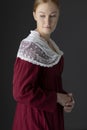 A Regency woman wearing a red linen dress with a lace modesty shawl against a studio backdrop