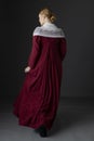 A Regency woman wearing a red linen dress with a lace modesty shawl against a studio backdrop