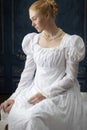 A Regency woman wearing a white cotton muslin dress and standing in a room