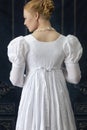 A Regency woman wearing a white cotton muslin dress and standing in a room