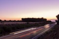 Regional road seen diagonally at sunset with light trail of cars driving in both directions