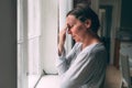 Regret and remorse, upset mid-adult female brunette standing by the the living room window in morning Royalty Free Stock Photo