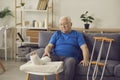 Sad senior man with broken leg sitting on sofa at home and thinking about his injury Royalty Free Stock Photo