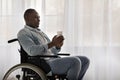 Serious adult african american guy disabled in wheelchair holds paper cup with hot drink