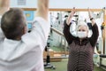Rehabilitation after coronavirus infection. Elderly woman in face medical mask do restorative exercises with a doctor in a gym dur
