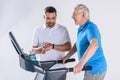 rehabilitation therapist checking time while assisting senior man exercising on treadmill Royalty Free Stock Photo