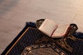 Rehal with open Quran and Muslim prayer beads on rug indoors