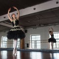 Rehearsal ballerina in the hall. White walls, dark wooden floor, dark ceiling, large mirrors. The reflection of the ballerina in