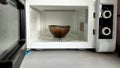 Reheating lunch in the microwave, black bowl of food in the microwave front view, open microwave