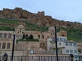 a reinforced concrete structure in a traditional city texture and the historical mardin castle in the background