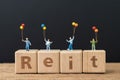 Reit, Real estate investment trust concept, happy miniature people holding balloons on cube wooden block with alphabet combine the