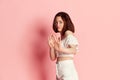 Rejection gesture. Young emotive pretty girl in white costume posing against pink studio background