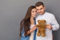 Relationship Concept. Young couple studio standing  on grey with teddy bear posing to camera cute Royalty Free Stock Photo