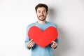Relationship and love concept. Handsome caucasian man in sweater holding big red valentines day heart cutout and smiling