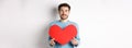 Relationship and love concept. Handsome caucasian man in sweater holding big red valentines day heart cutout and smiling