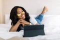 Relax and beauty procedures on weekend. Pleasant African smiling woman lying on bed in cozy room, with golden eye Royalty Free Stock Photo