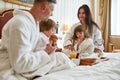 Relax and feel peace. Close up of parents and two kids in white bathrobes having breakfast in bed, eating and drinking Royalty Free Stock Photo