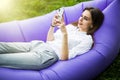 Relax on fresh air. Pretty young woman lying on inflatable sofa lamzac use mobile phone while resting on grass in park on the sun Royalty Free Stock Photo