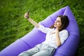 Relax on fresh air. Pretty young woman lying on inflatable sofa lamzac use mobile phone while resting on grass in park on the sun Royalty Free Stock Photo